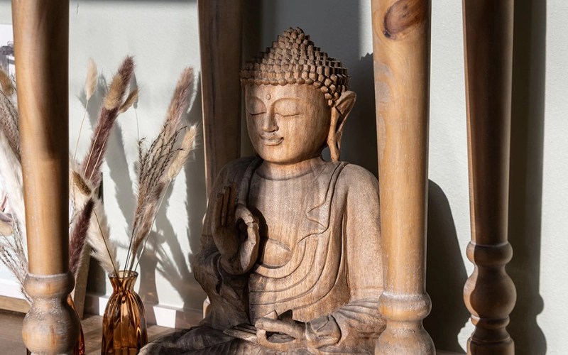 Carved wooden Buddha statue beside dried pampas grass in an amber vase at Glow Hot Yoga Sarasota