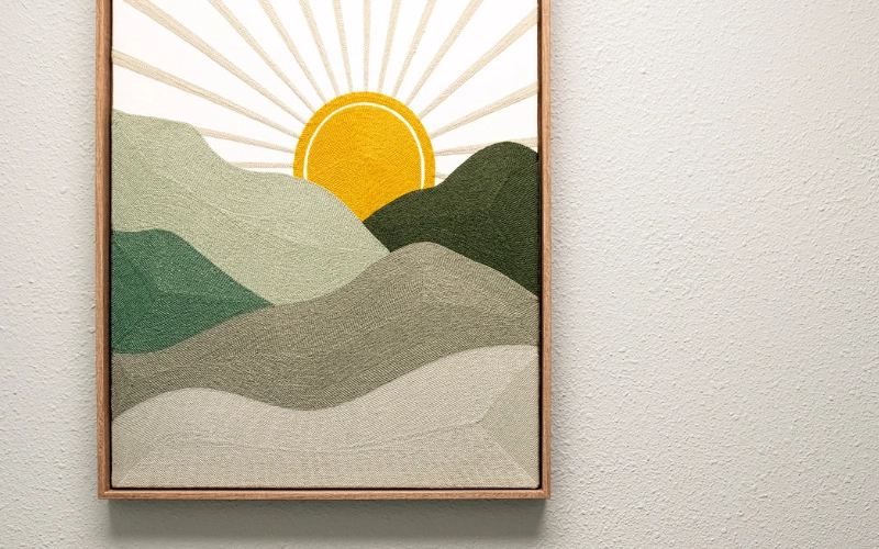 Framed textile wall art of a sunrise over mountains hanging inside Glow Hot Yoga Sarasota